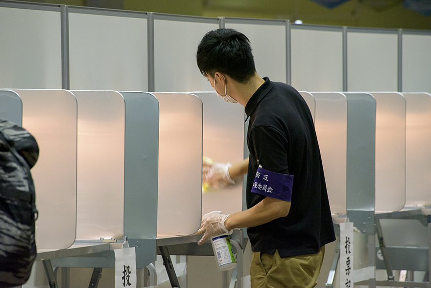 Image of a polling station employee disinfecting a booth