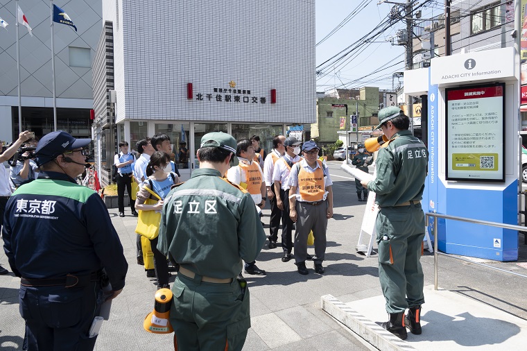 Photo: Training to guide people gathering in front of the signage at the East Exit of Kitasenju Station