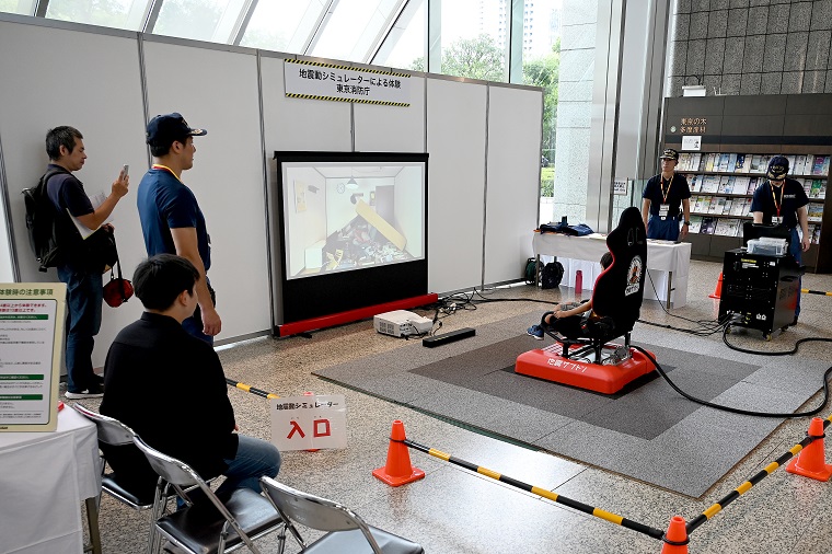 体験者が椅子に座り、正面のスクリーン映像と共に地震を体験する画像